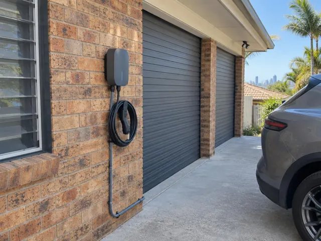 Wall-mounted EV charger and coiled cable on a brick garage wall beside a driveway in Mermaid Beach
