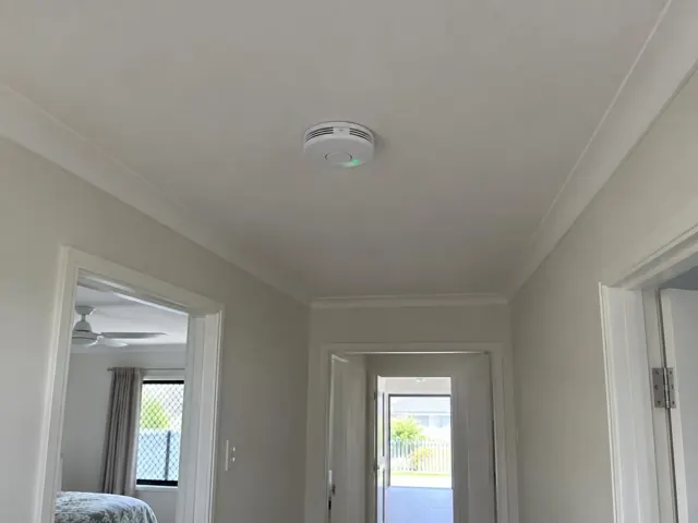 Ceiling smoke alarm in a white hallway with doorways and a bedroom visible in Broadbeach